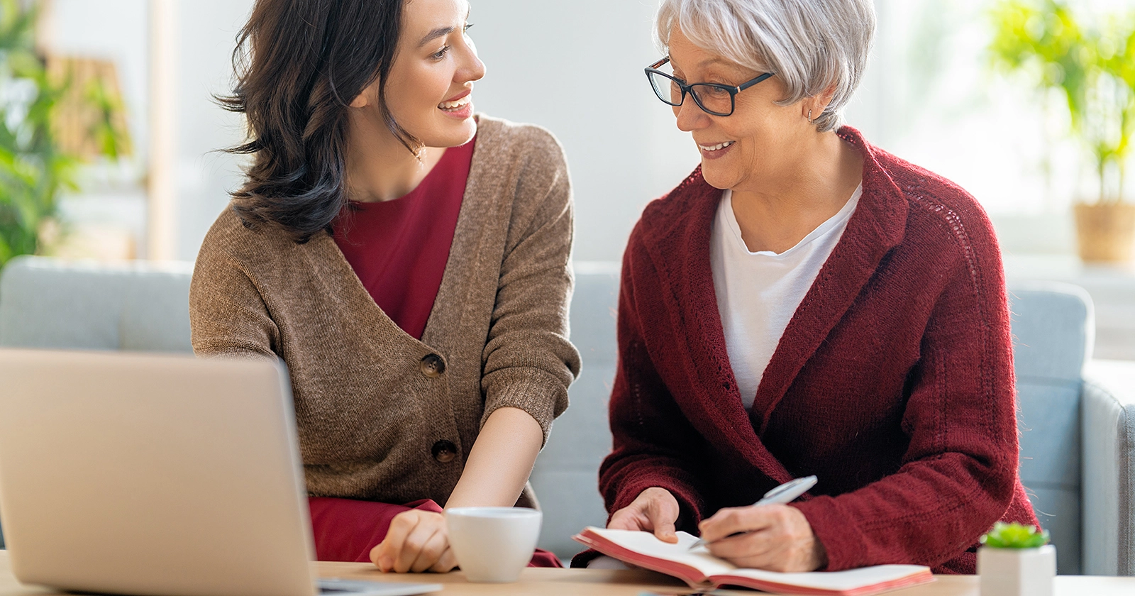 Two women talking, one on a laptop while the other takes notes